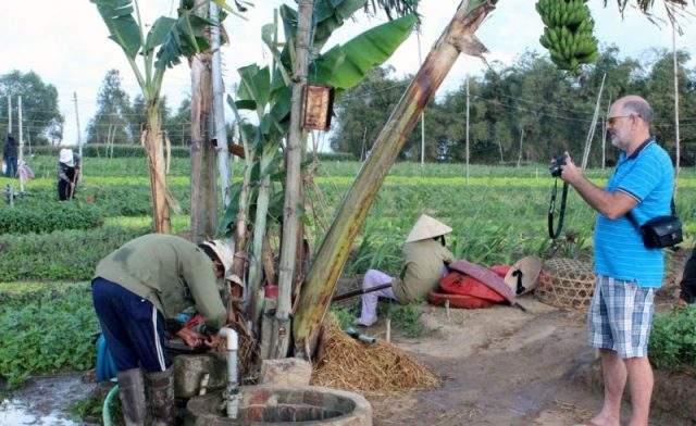 Du khách nước ngoài chụp lại hình ảnh người nông dân chuẩn bị máy bơm nước tưới rau (Ảnh Collection)